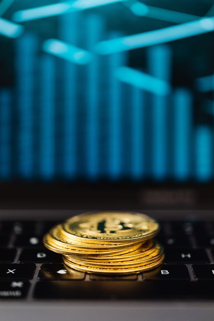 Close-up of gold Bitcoin coins stacked on a laptop keyboard with a digital chart reflection.