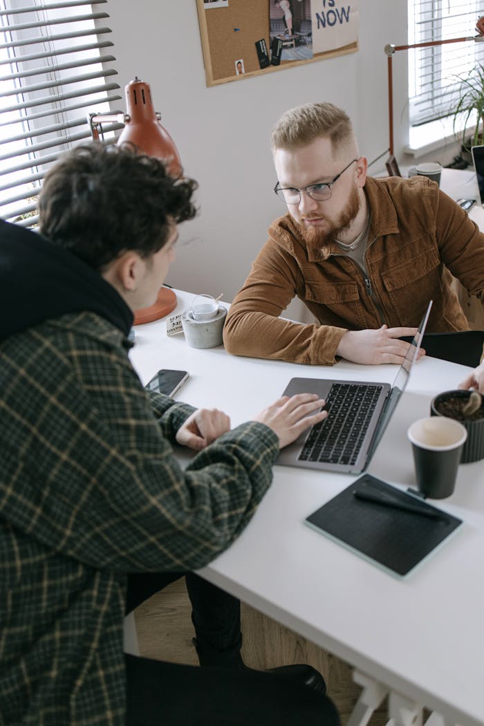 Two young men in a modern office discuss a project using a laptop. Creative team meeting.